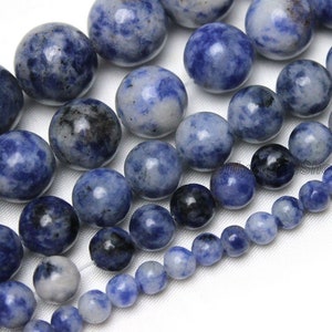Op de afbeelding: Een streng blauwe en witte edelsteen kralen. De kralen zijn rond en hebben een gevlekte uitstraling. De kralen zijn van verschillende grootte, waarbij de grootste kralen ongeveer 2,5 cm in diameter zijn.