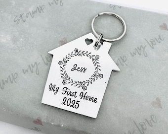 May include: Silver house-shaped keychain with a floral wreath design and the text "My First Home 2025". The wreath has the name "Jess" in the center.