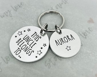 May include: Silver keychain with two tags. One tag says "This Uncle Belongs To..." with stars around the text. The other tag says "Aurora" with a star below the text.