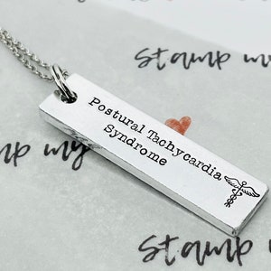 May include: Silver necklace with a rectangular pendant that reads "Postural Tachycardia Syndrome" with a medical symbol.