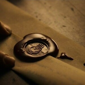 May include: A brown wax seal with a handprint design on a brown envelope.