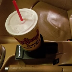 May include: A close-up of a cup holder in a car with a red straw sticking out of a white cup with a yellow and red logo that says "Bojangles Famous Chicken 'n Biscuits".