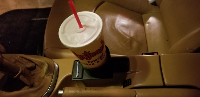 May include: A close-up of a cup holder in a car with a red straw sticking out of a white cup with a yellow and red logo that says "Bojangles Famous Chicken 'n Biscuits".