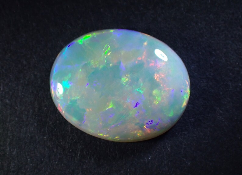 May include: A white opal gemstone with a light blue body colour and iridescent flashes of green, purple, and pink.