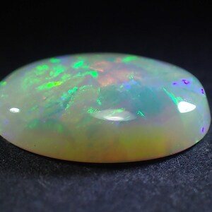 May include: A white oval opal gemstone with green and purple iridescence.
