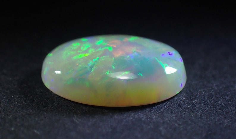 May include: A white oval opal gemstone with green and purple iridescence.
