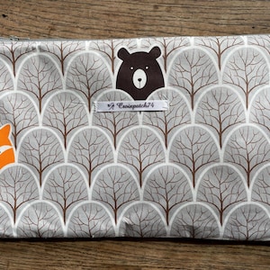 Pode incluir: Uma bolsa retangular com zíper com um padrão repetido de árvores cinzentas com galhos marrons. A bolsa tem um urso marrom e duas raposas laranja. O texto "/ Croixpatch74" está em uma etiqueta branca.
