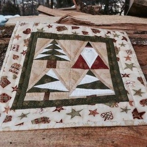 May include: A square Christmas-themed quilted table topper. The centre features two Christmas trees and two Santa Claus figures. The border is decorated with stars, hearts, and gift motifs. The colour palette includes beige, green, red, and white.
