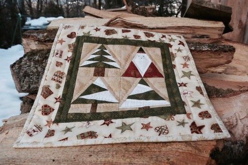 May include: A square Christmas-themed quilted table topper. The centre features two Christmas trees and two Santa Claus figures. The border is decorated with stars, hearts, and gift motifs. The colour palette includes beige, green, red, and white.