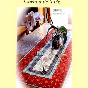 Peut inclure: Chemin de table rouge &agrave; motifs floraux, avec un motif floral brod&eacute; au centre, bord&eacute; de rayures bleues et grises. Le chemin de table mesure 124x44cm. Le texte "CROIX PATCH 74" et "Chemin de table" sont en haut.