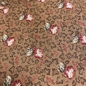 Peut inclure: Gros plan sur un tissu marron avec un motif floral. Le motif présente de petites feuilles brun foncé et des fleurs dans des tons de rouge, crème et marron. Le tissu a un aspect texturé, suggérant un matériau tissé.