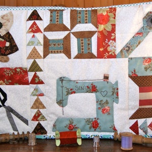 Peut inclure: Une courtepointe patchwork avec des motifs de couture. Le design comprend une machine à coudre, des bobines de fil, des ciseaux et une figurine en bonnet. La palette de couleurs comprend le blanc, le sarcelle, le rouge et le marron. Le mot "SINGER" est visible sur la machine à coudre.