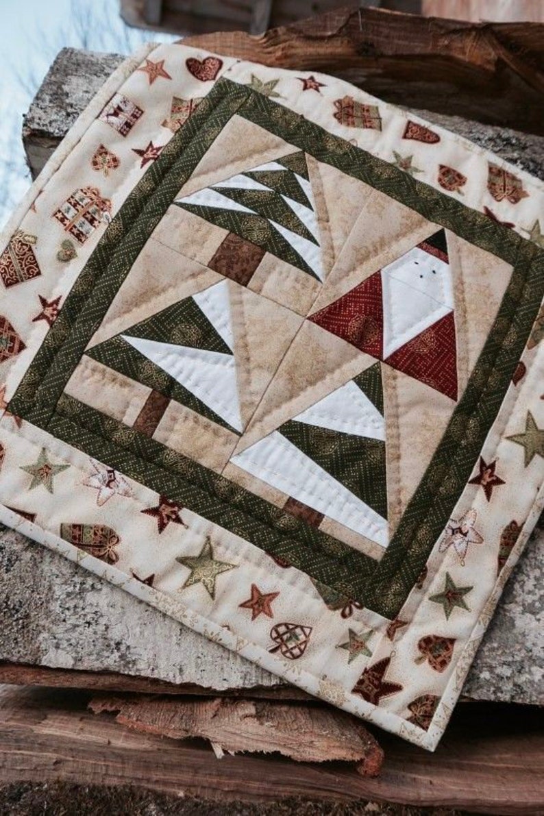 May include: A festive quilted placemat with a Christmas theme. The central design features stylized Christmas trees and a Santa Claus figure. The border is decorated with stars, hearts, and gift box patterns in green, red, and beige.