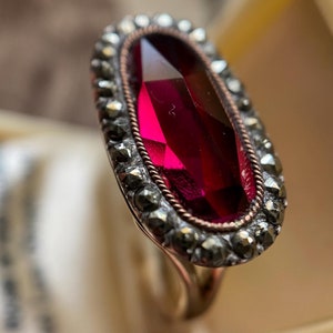 May include: A vintage ring with a large, faceted, ruby red stone set in a silver and marcasite setting.