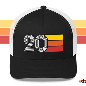 May include: A black trucker hat with a white mesh back. The front of the hat features a white retro-style graphic of the number "20" with a multi-coloured stripe design.