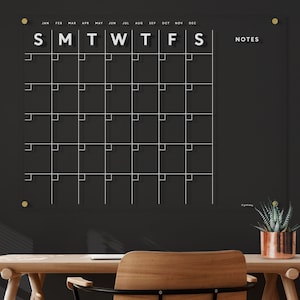 May include: A black dry erase calendar with white grid lines and white text. The calendar has the months of the year listed across the top and the days of the week listed below. The words "NOTES" are written in white on the right side of the calendar.