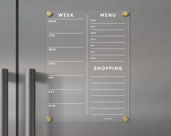 May include: A clear acrylic magnetic planner board featuring white printed text for a weekly schedule, menu, and shopping list. The board is secured with four gold-toned circular hardware mounts at the corners, displaying days of the week.