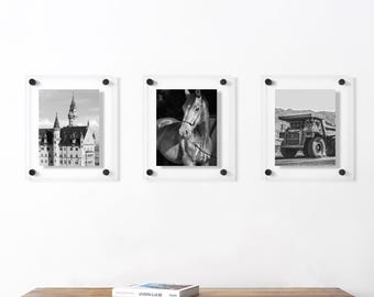 May include: Three square acrylic floating picture frames mounted in a horizontal row. Each frame features black hardware at the corners and displays a black and white photograph: a castle, a horse, and a large industrial mining dump truck.