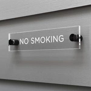 May include: A clear acrylic sign with black standoffs reads "NO SMOKING" in white lettering.