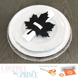 May include: Black felt maple leaf napkin ring. The napkin ring is on a white plate with a silver charger. The text "Convince the Prince" is visible in the bottom left corner of the image. The text "Can be made by scissors only!" is visible in the bottom right corner of the image.