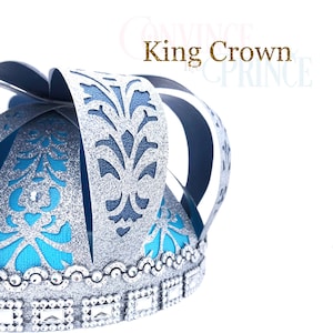 May include: A silver and blue paper crown with a glitter finish and a blue and silver patterned design. The crown has a silver trim with rhinestones.