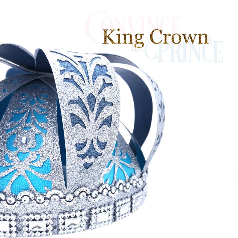 May include: A silver and blue paper crown with a glitter finish and a blue and silver patterned design. The crown has a silver trim with rhinestones.