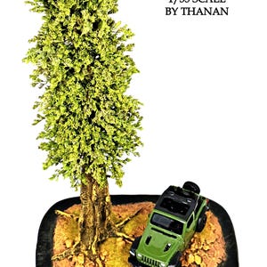 Könnte beinhalten: Ein 1/35 Modellbaum von Thanan, bestehend aus einem hohen, strukturierten grünen Baum mit braunem Stamm, neben einem kleinen grünen Geländewagen auf einem strukturierten braunen Untergrund mit Steinen und grünen Moosflecken.
