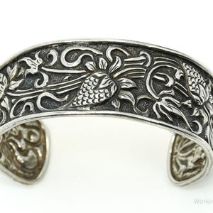 May include: Silver cuff bracelet with an intricate floral design. The bracelet is made of sterling silver and features a detailed floral pattern.