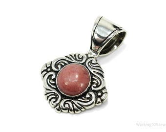 May include: A silver pendant with a round, pink gemstone center. The pendant has an ornate, swirling design around the gemstone and a silver bail for a chain. The jewelry piece is likely a necklace pendant.