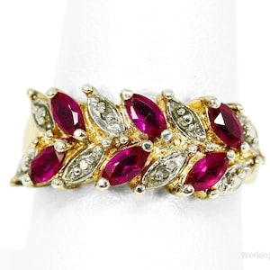 May include: A gold ring featuring marquise-cut ruby gemstones and small diamond accents. The ring's design resembles a series of leaves or petals, with the rubies set in a row. The ring is displayed on a white background.