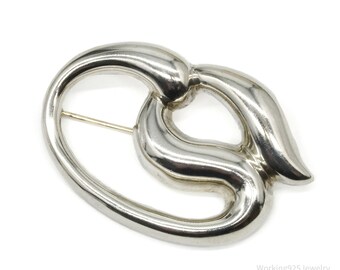 May include: A silver brooch with an abstract, flowing design. The brooch has a polished, reflective surface and a pin fastening. The design is a modern, intertwined shape, suitable for adding a touch of elegance to any outfit.