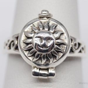 Op de afbeelding: Een zilveren ring met een lachend zonontwerp. De ring heeft een rond gezicht met een lachende zon en decoratieve krullen op de band. De ring is gemaakt van sterling zilver.