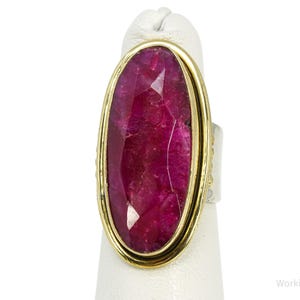 May include: An oval ring featuring a large, faceted, deep magenta-colored stone set in a gold-toned metal bezel. The ring band is silver-toned, and the text Working925Jewelry is visible in the bottom right corner of the image.
