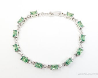 May include: A silver bracelet featuring a delicate chain and rectangular green gemstones. The bracelet has a clasp fastening.