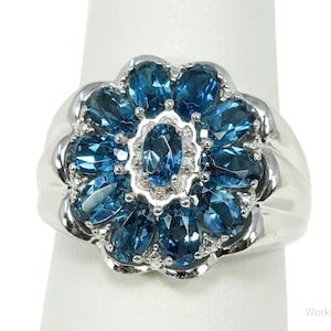 Puede incluir: Anillo de plata con diseño floral, engastado con piedras preciosas azules ovaladas y en forma de pera. El anillo tiene una banda de plata pulida y las piedras están dispuestas en forma de pétalo.