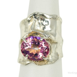 Peut inclure: Bague en argent ornée d'une grosse pierre rose ovale. La bague présente un design texturé et organique autour de la pierre, créant un bijou unique. La pierre précieuse possède de multiples facettes qui réfléchissent la lumière.