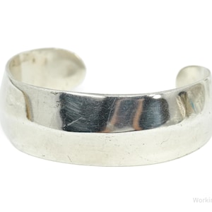 Op de afbeelding: Een zilveren manchetarmband met een breed, gebogen ontwerp. De armband heeft een gladde, gepolijste afwerking en een eenvoudige, elegante stijl. Het open ontwerp maakt het gemakkelijk te dragen. Een klassiek sieraad.
