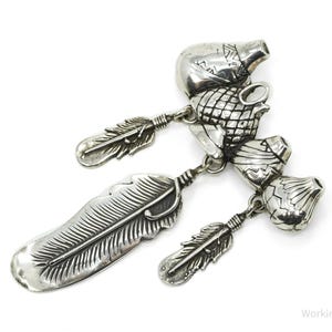 Puede incluir: Un colgante plateado con dijes detallados, que incluyen un pájaro, plumas y otros elementos decorativos. El colgante probablemente está hecho de plata de ley y se muestra sobre un fondo blanco. El diseño es intrincado y llamativo.