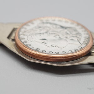 May include: A silver money clip holding a silver coin with a copper-colored rim. The coin features a profile of a woman and the year 1890. The money clip has a rectangular design with cut-out details.