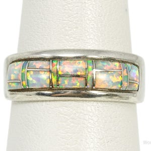 May include: A silver band ring featuring a horizontal inlay of rectangular iridescent opal segments. The opal pieces display flashes of green, orange, and pink colours, separated by thin silver dividers within the polished metal setting.
