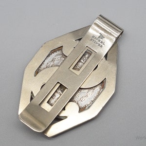 May include: Silver-toned money clip with a geometric design. The clip features a rectangular bar with the words "Nickel Silver" stamped on it. The clip is designed to hold currency or cards.
