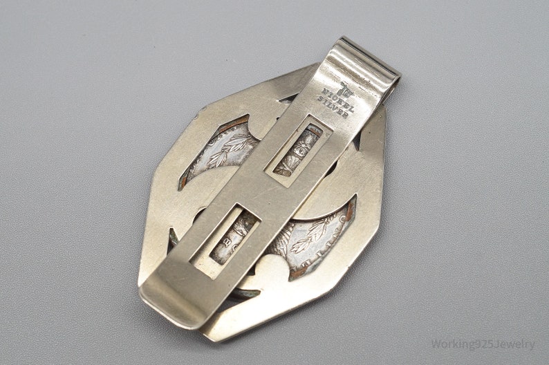 May include: Silver-toned money clip with a geometric design. The clip features a rectangular bar with the words "Nickel Silver" stamped on it. The clip is designed to hold currency or cards.