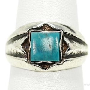 May include: A silver ring with a square turquoise stone set in the center. The ring has a wide band with etched details and a decorative setting around the stone. The turquoise stone is a vibrant blue-green color.