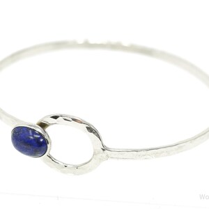 May include: A silver bangle bracelet with a hammered finish and a blue lapis lazuli stone set in a circle.