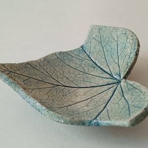 Könnte beinhalten: Eine Keramik-Schale in Blattform mit hellblauer Glasur und weißer Craquelé-Oberfläche. Die Schale ist so gestaltet, dass sie einem echten Blatt mit Adern und einer strukturierten Oberfläche ähnelt.