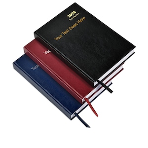 May include: Three stacked hardcover diaries in black, burgundy, and navy. The top diary is black with gold text reading "2026 Day a Page Diary" and "Your Text Goes Here." Each diary has a ribbon bookmark in a matching colour.