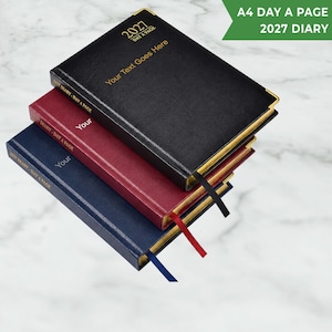 May include: A stack of three A4 day-a-page 2027 diaries in black, burgundy, and navy blue. Each diary features gold-coloured corner protectors, gold-edged pages, and a matching ribbon bookmark. The covers are imprinted with 2027 and Your Text Goes Here.