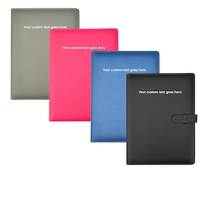 May include: Four leather-bound journals in grey, pink, blue, and black. Each journal has the text "Your custom text goes here" printed in white. The black journal has a strap closure.