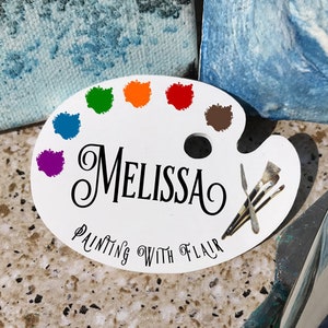 May include: White ceramic paint palette with a colorful paint swatch design. The palette has the name "Melissa" and the text "Painting with Flair" written on it.