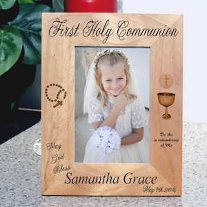 May include: A wooden picture frame with a light brown finish. The frame has a cutout of a rosary and a chalice with a cross on top. The frame has the text "First Holy Communion", "May God Bless", "Samantha Grace", "Do this in remembrance of Me", and "May 7th 2016".